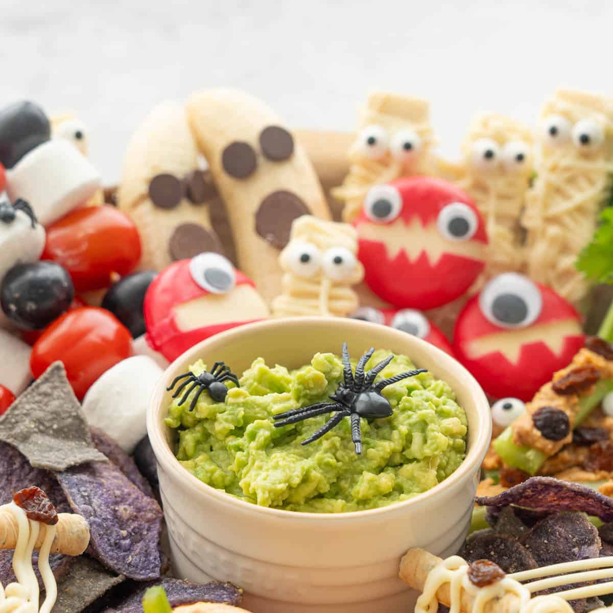 Halloween monsters together, two banana ghosts, three mummy wafers cookies, cheese monsters and guacamole with fake spiders on top.