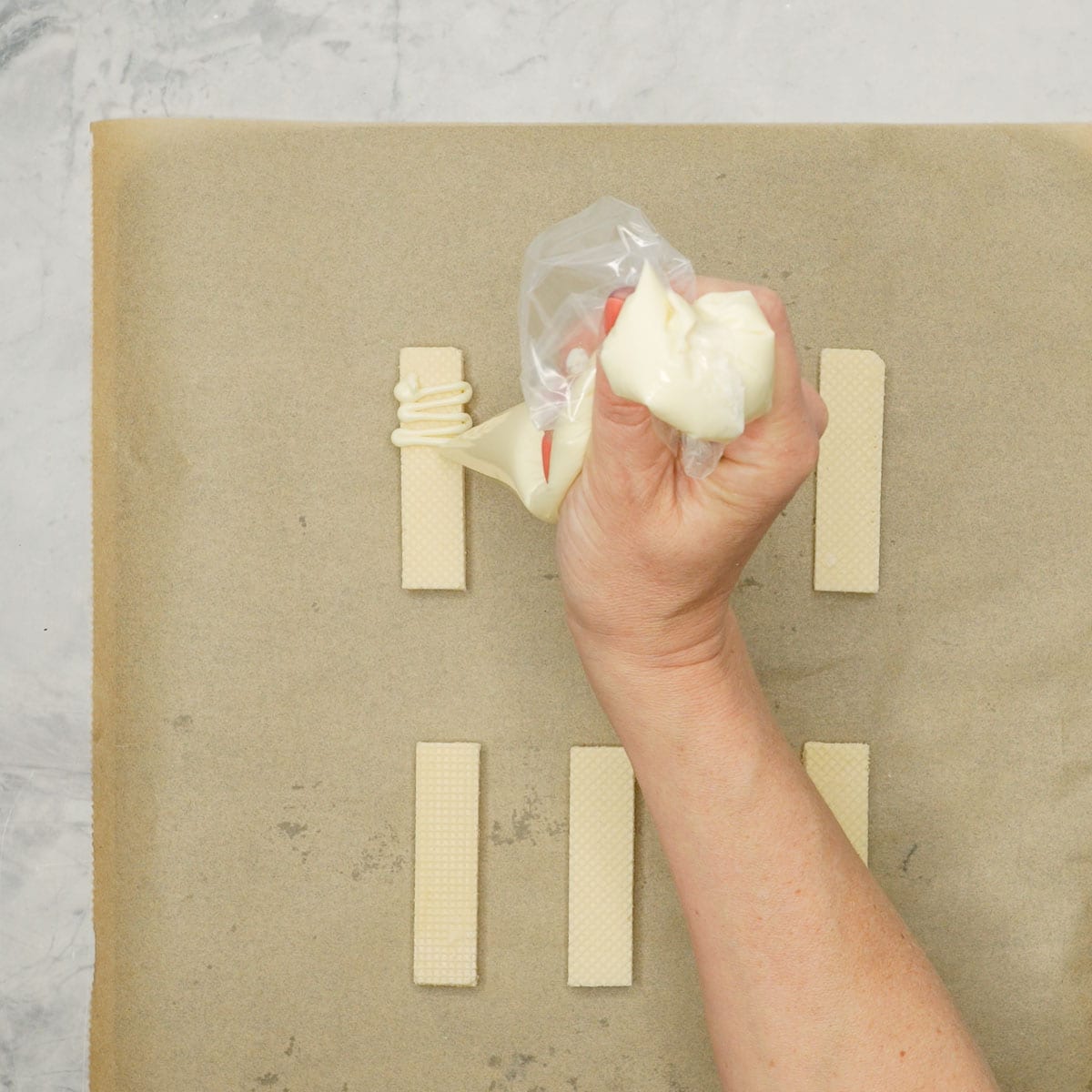 Hand holding a piping bag with melted white chocolate inside, drizzling back and forward over wafer stick.