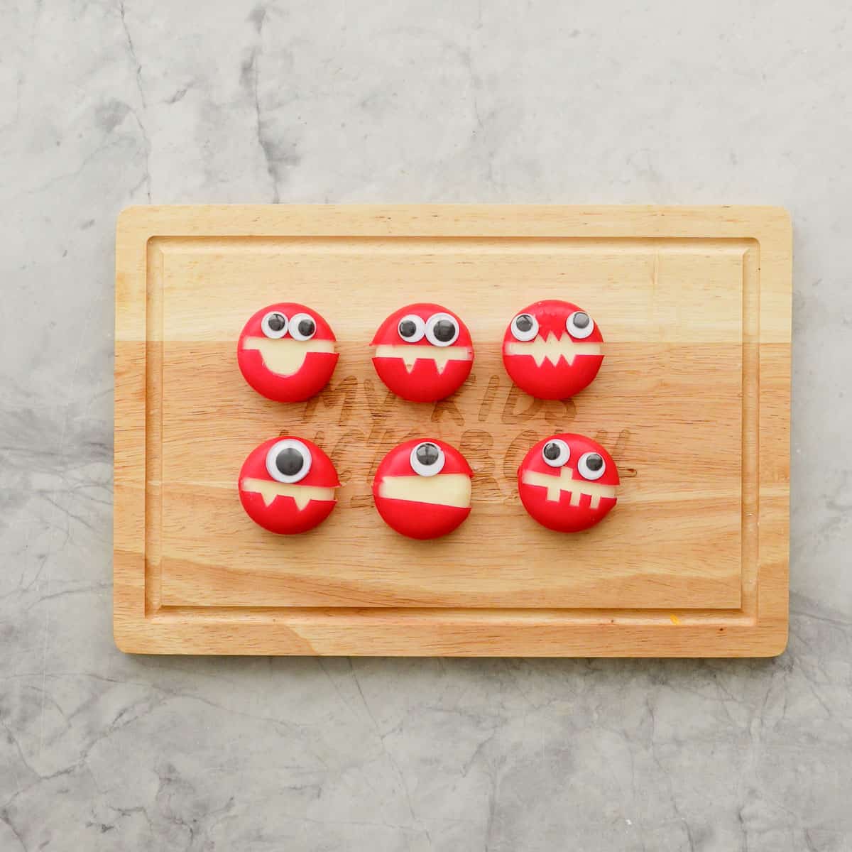 Cheese Monsters on wooden chopping board, googly eyes and mouths cut out.