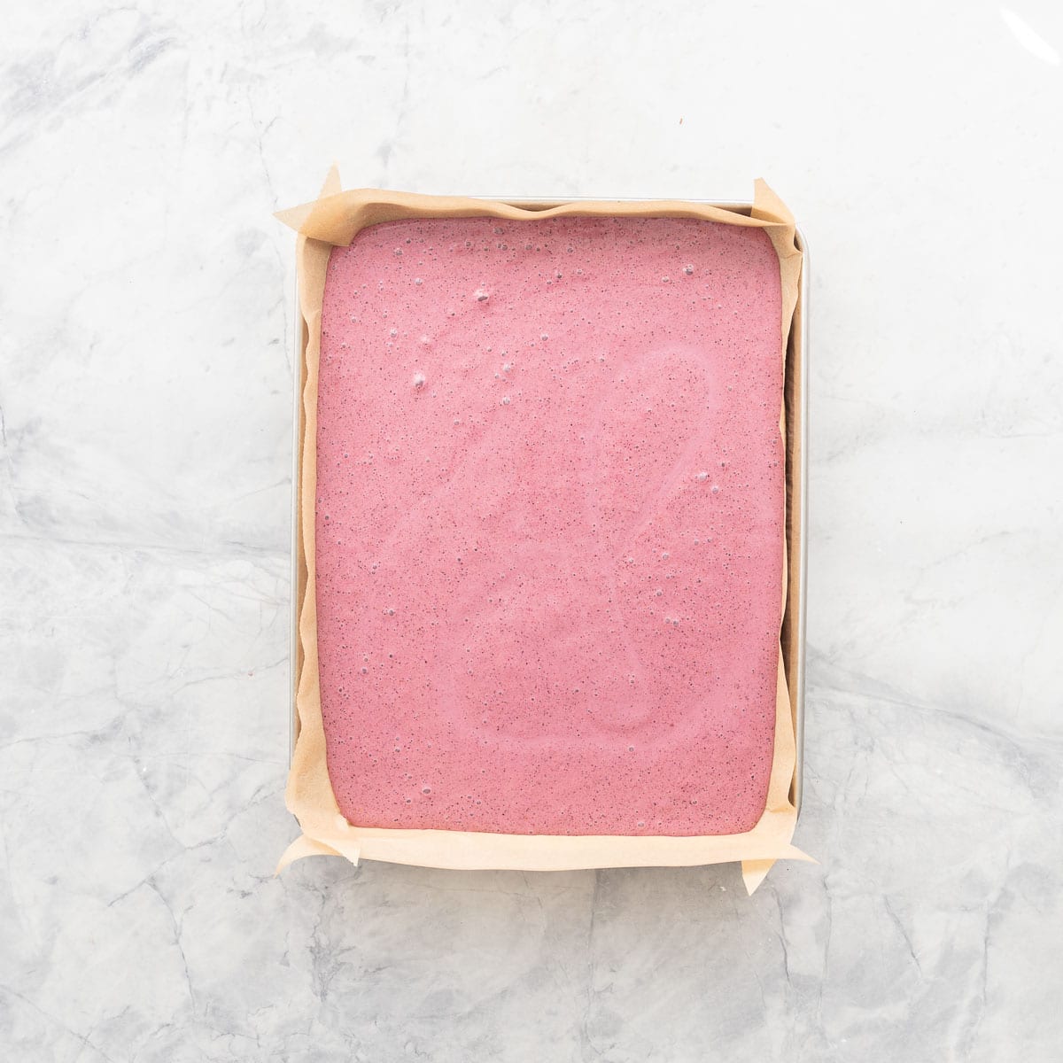 Blended berry yogurt mixture poured into a lined baking tray on bench top.