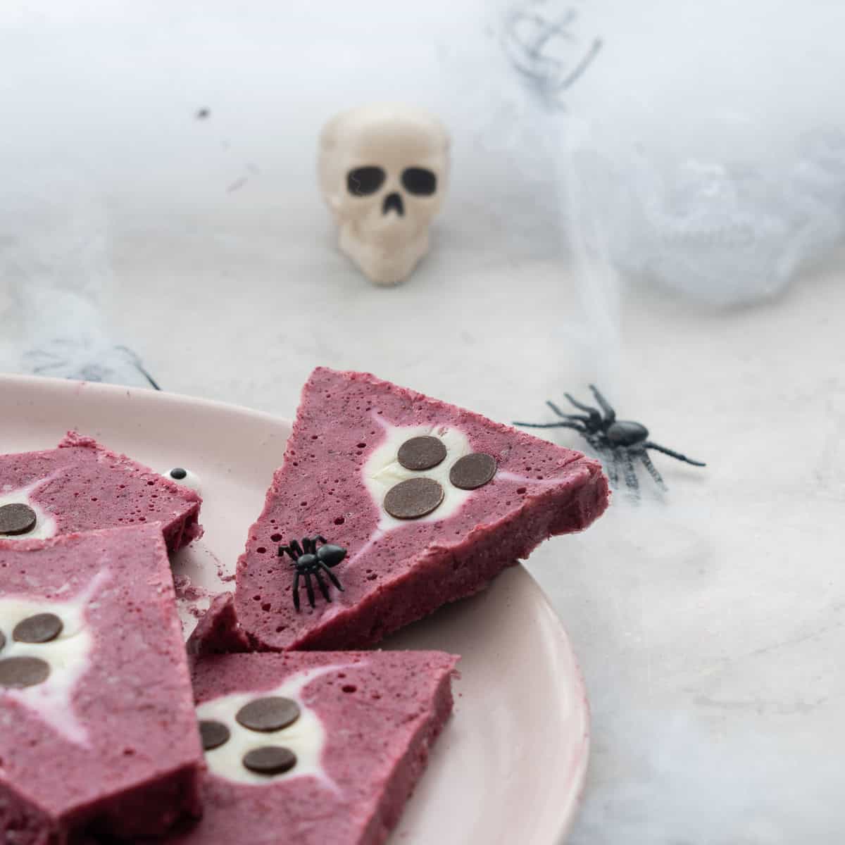 Frozen Halloween yogurt bark broken into pieces on a plate with fake spiders crawling on top and on benchtop.