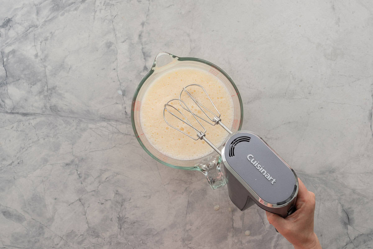 Wet ingredients in bowl being whisked with electric hand beater.