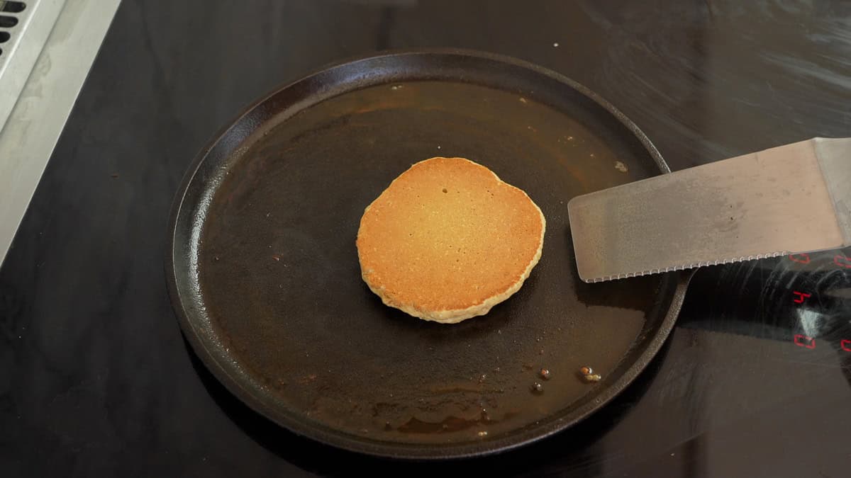 Oat flour pancake on flat pan cooked side up slightly browned and spatula resting on pan.