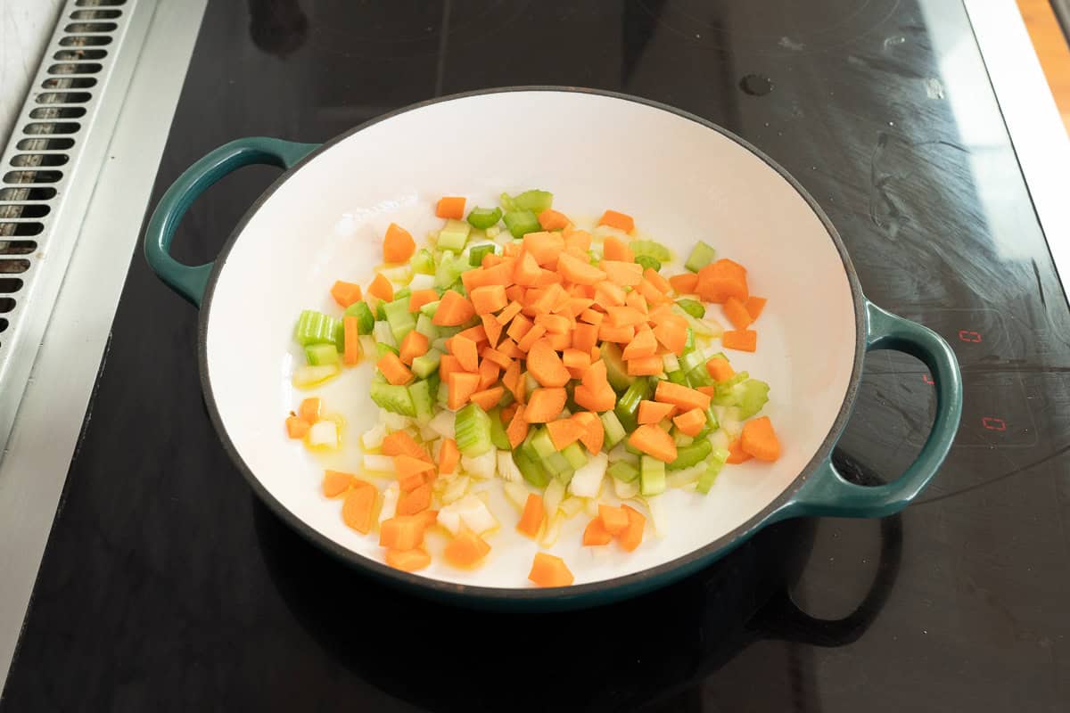 Chopped onion, celery and carrot in cast iron pan on bench top sautéing.