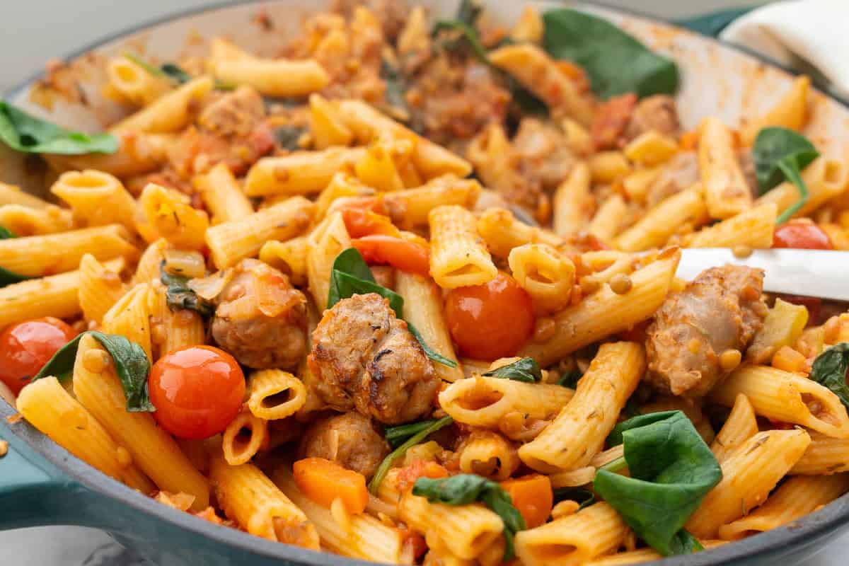 Sausage pasta in cast iron pan placed on benchtop.