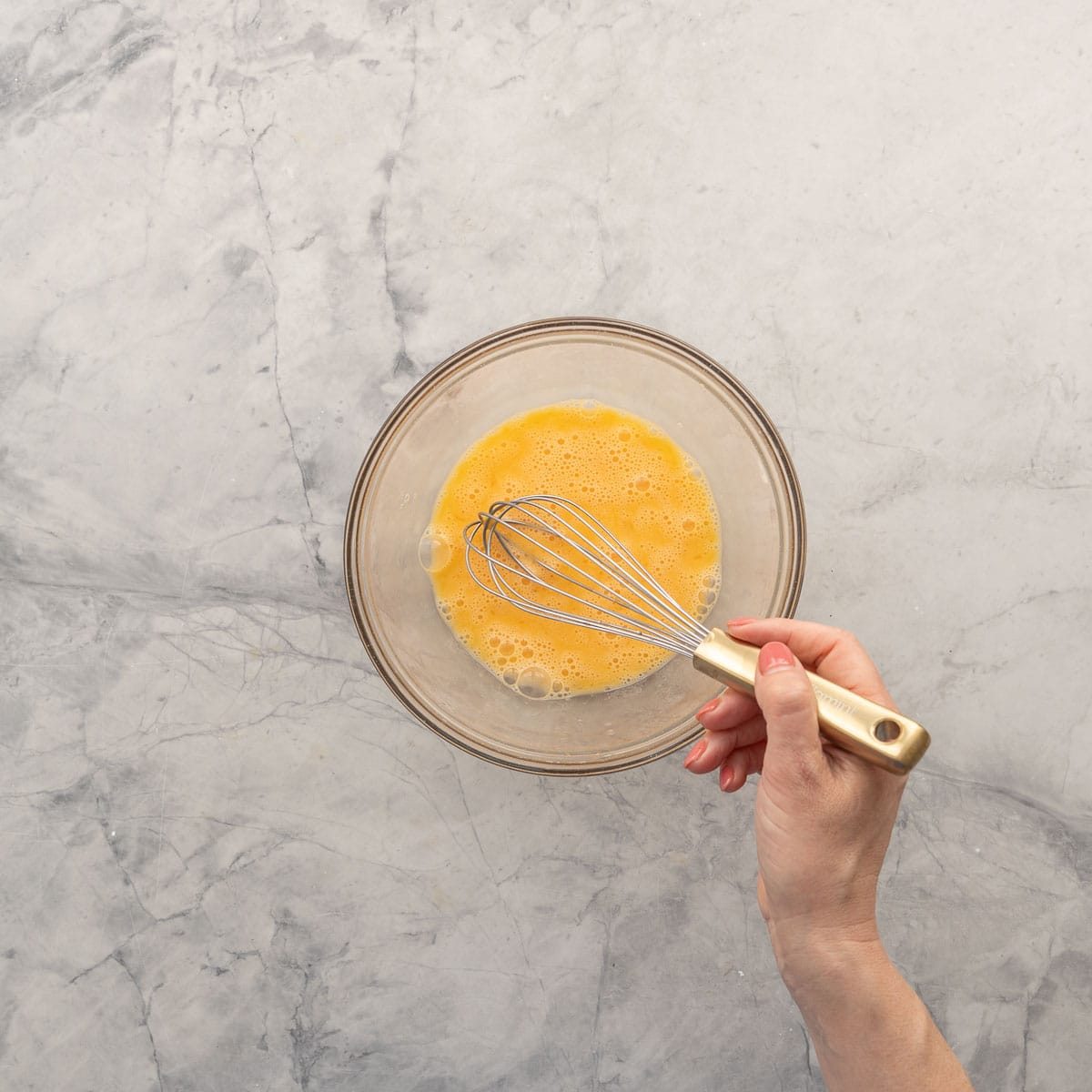 Eggs in a glass bowl on bench top being whisked together.