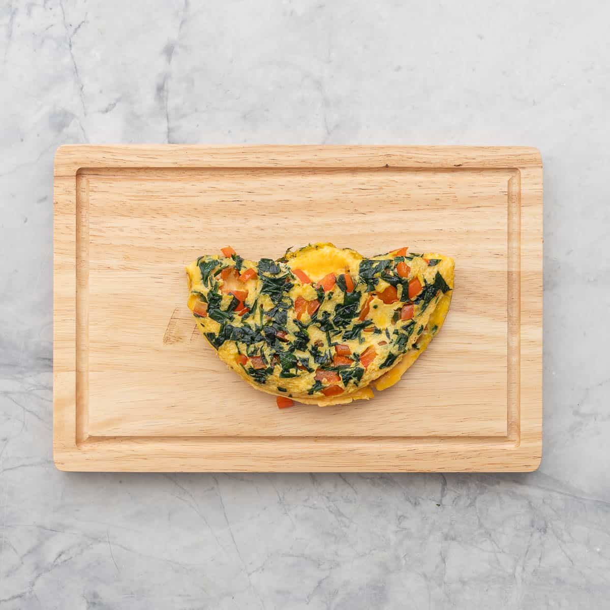 Spinach omelette folded in half on placed on chopping board.