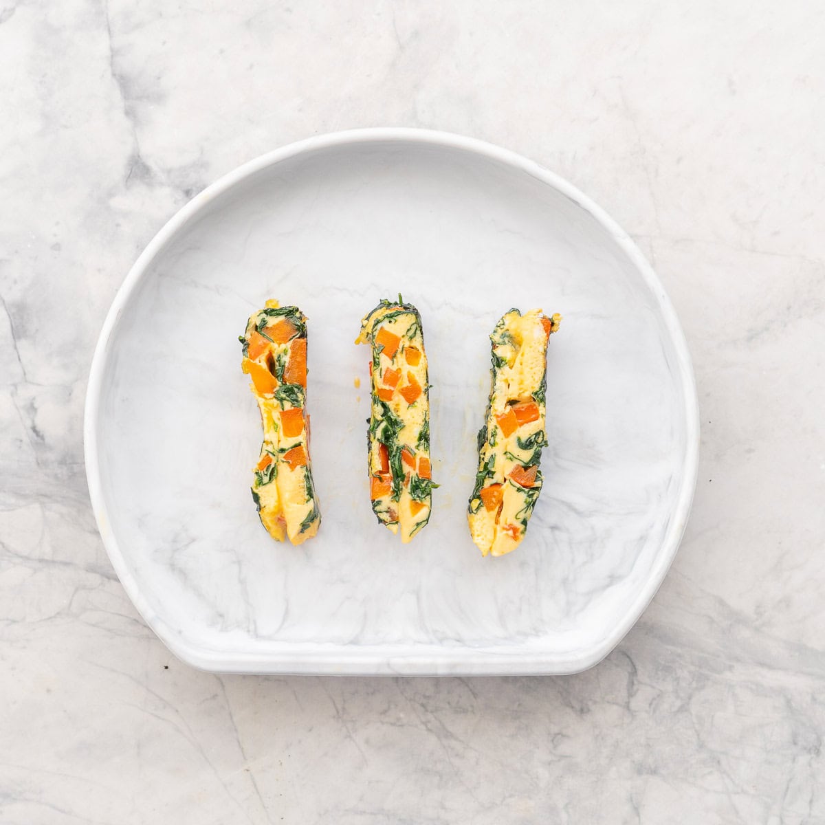 Spinach omelette cut into strips on silicone childs plate.