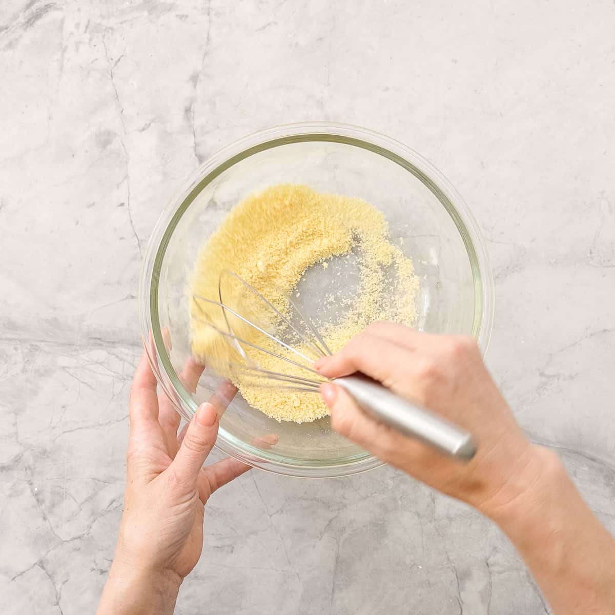 Cheese in glass bowl on bench top being whisked.