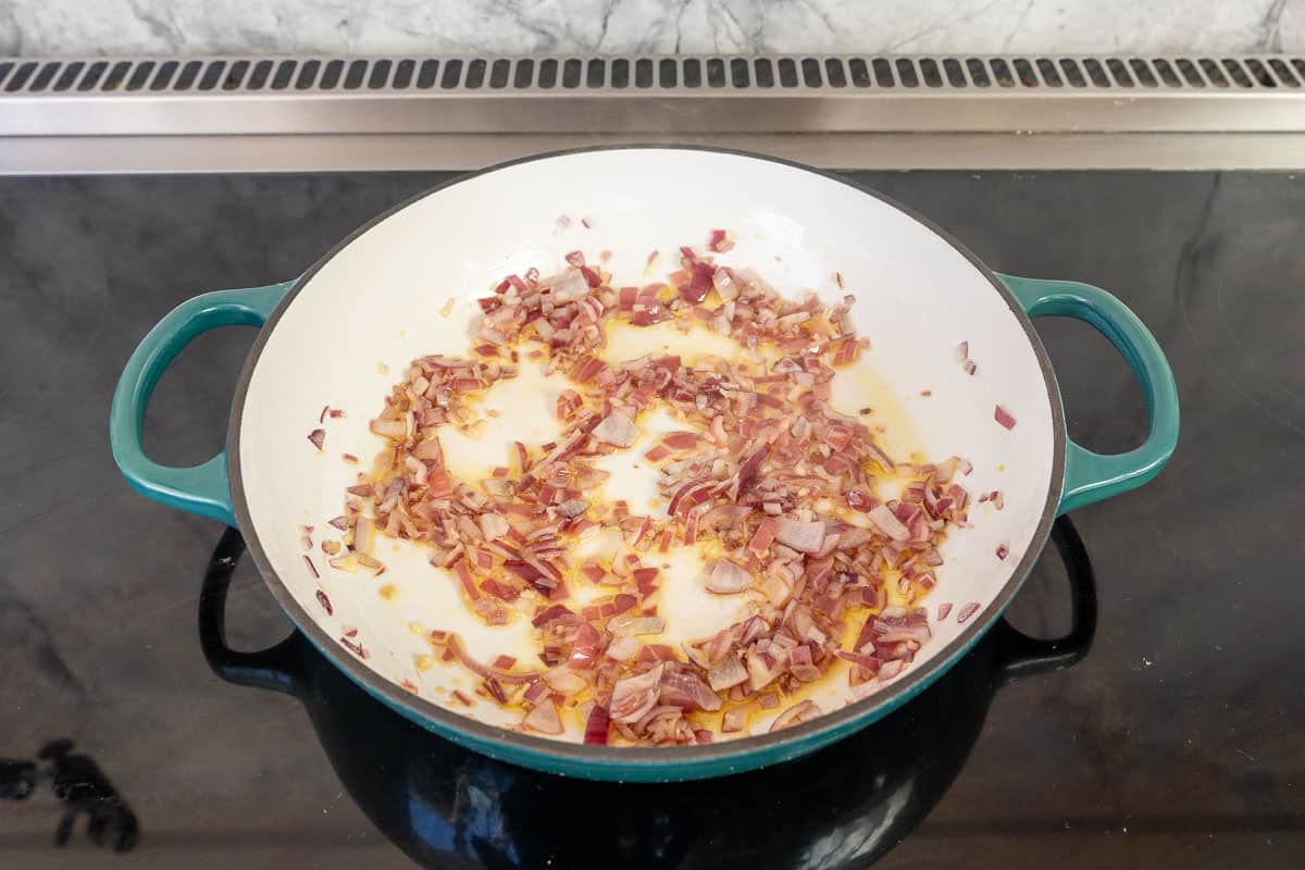 Oil and red onion in skillet on stove top sautéing.