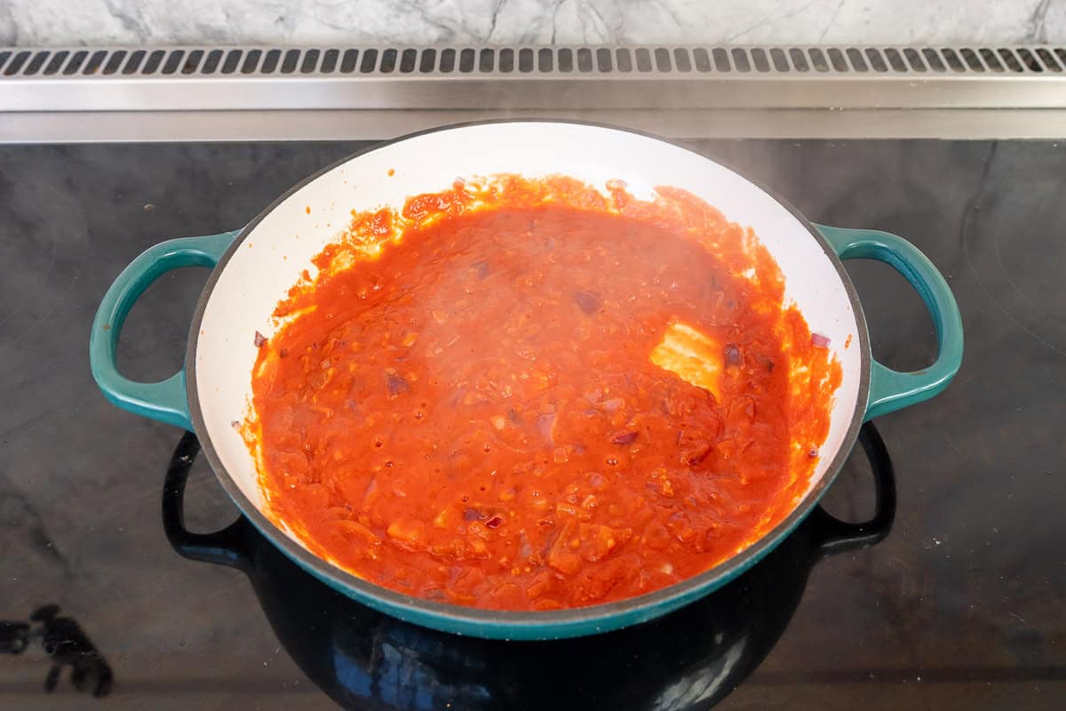 Tomato Puree added into oil and red onion in skillet on stove top.