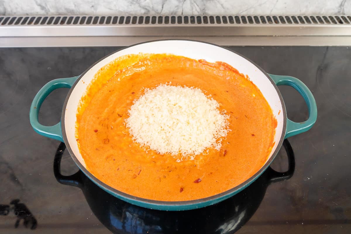 Skillet on stove top with creamy tomato sauce simmering, parmasan cheese added on top of sauce mixture.