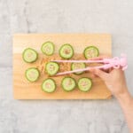 Tuna and Rice mixture stuffed inside hollowed out cucumber pieces on a chopping board, pink child chopsticks picking up a piece.