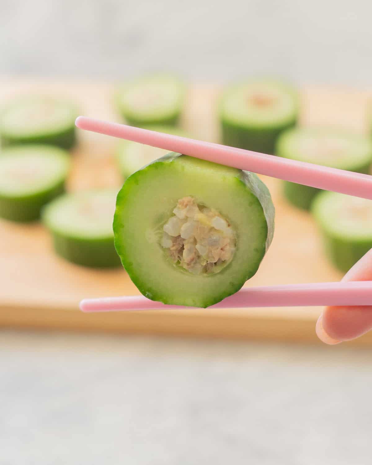 Tuna and Rice mixture stuffed inside hollowed out cucumber piece being held by chopstick showing the filling.