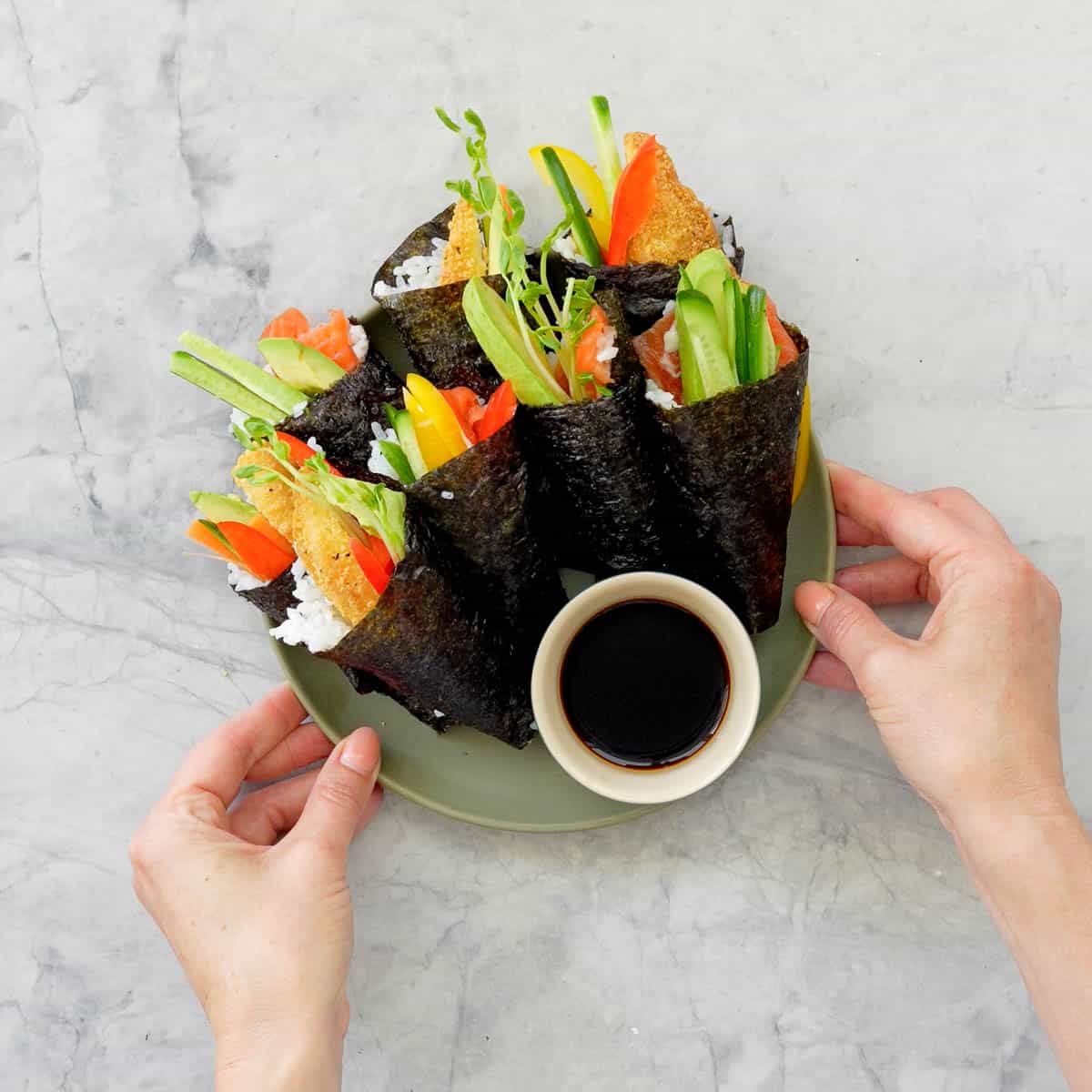 Hand roll sushi pieces on a plate with dish of soy sauce.