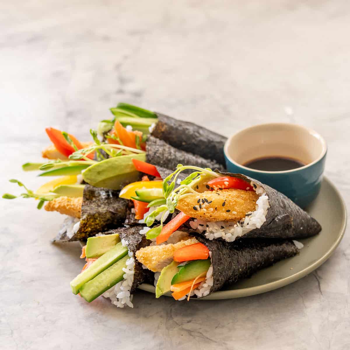 Hand roll sushi pieces on a plate with dish of soy sauce.