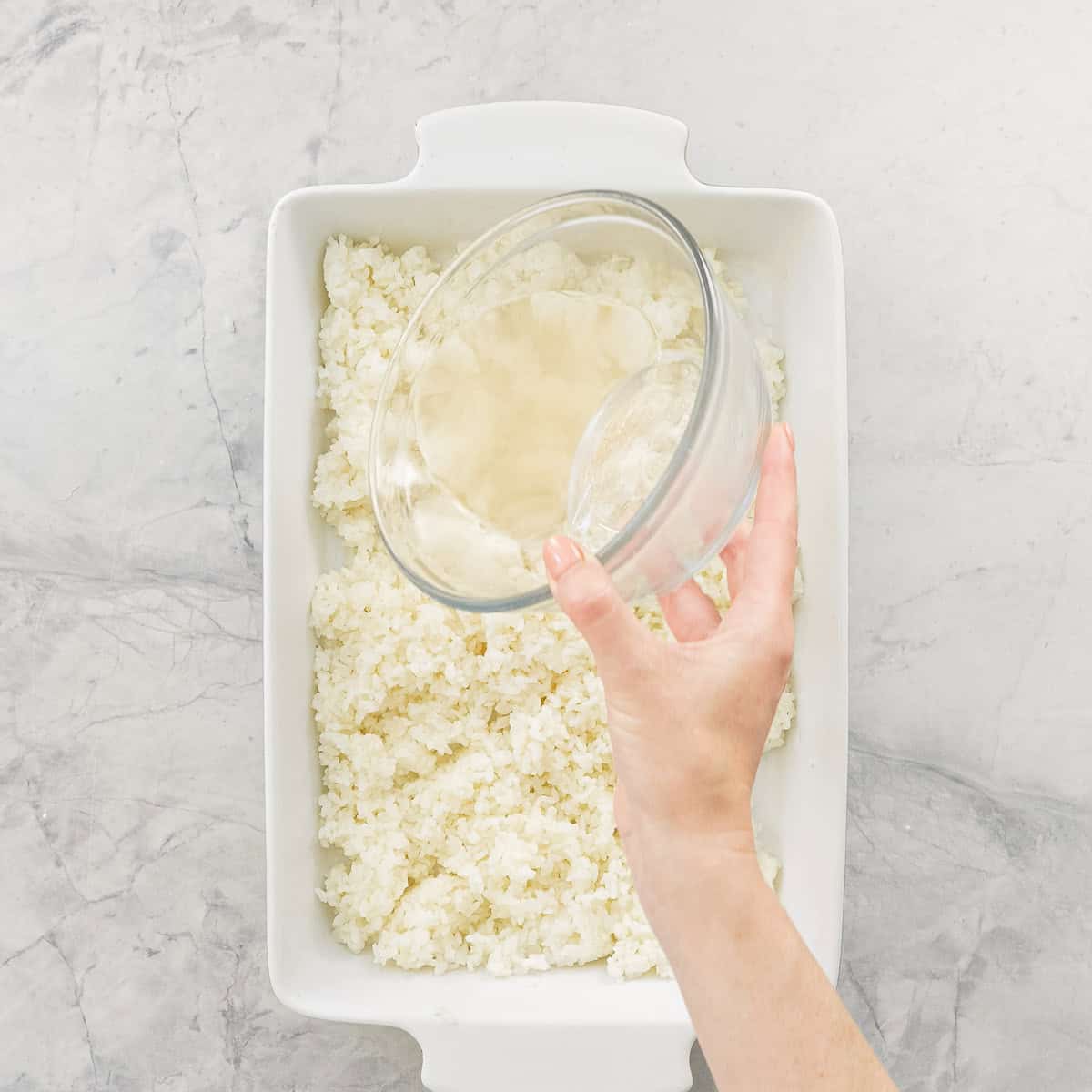 Vinegar Mixture being poured over a shallow dish of cooked rice.