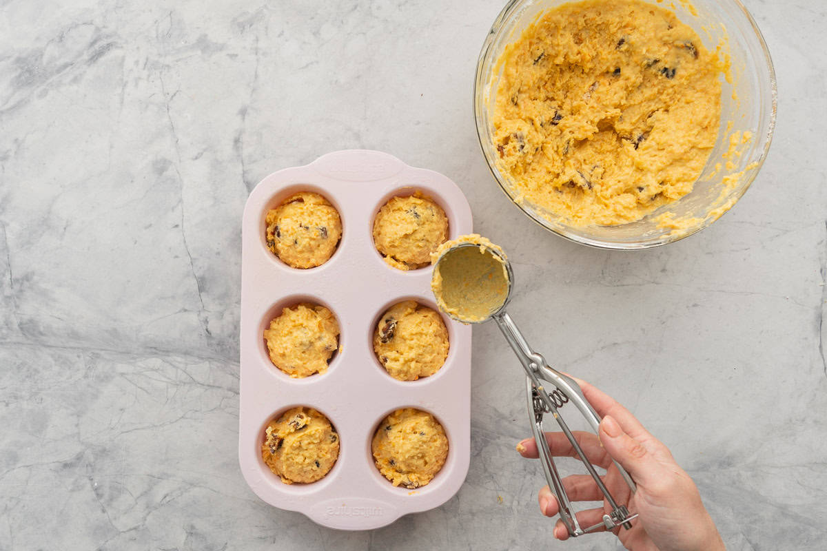 Cookie scooper scooping portions from Mandarin muffin mixture into silcone muffin tray.