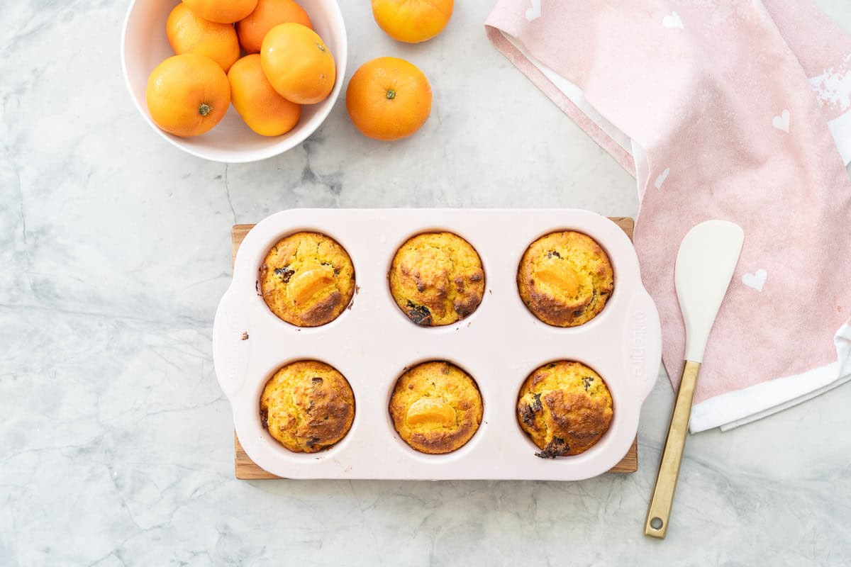 Mandarin muffins cooked in silicon muffin tray on bench top with fruit bowl of mandarins in background.