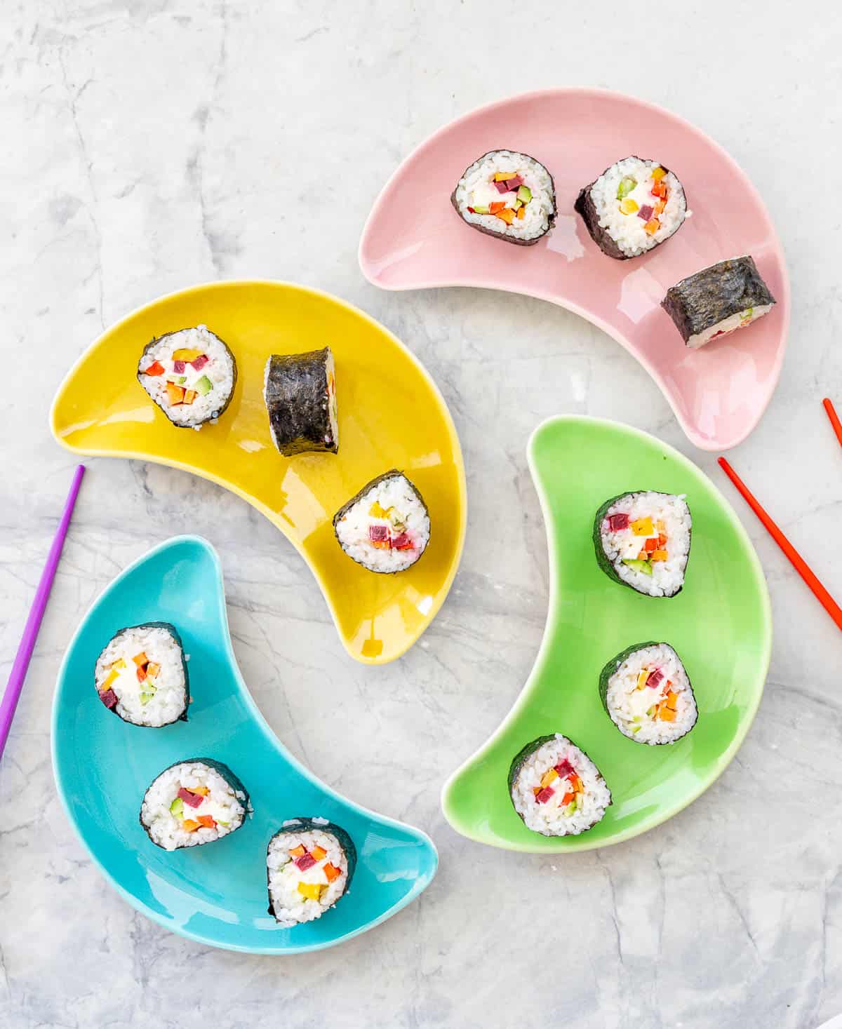 Four moon shaped colourful plates on bench top with rainbow sushi showing ingredients inside.