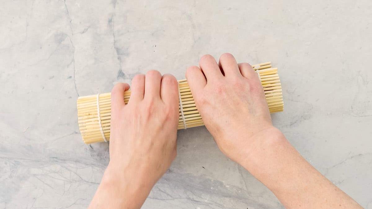 Hands holding sushi mat rolled into a log.