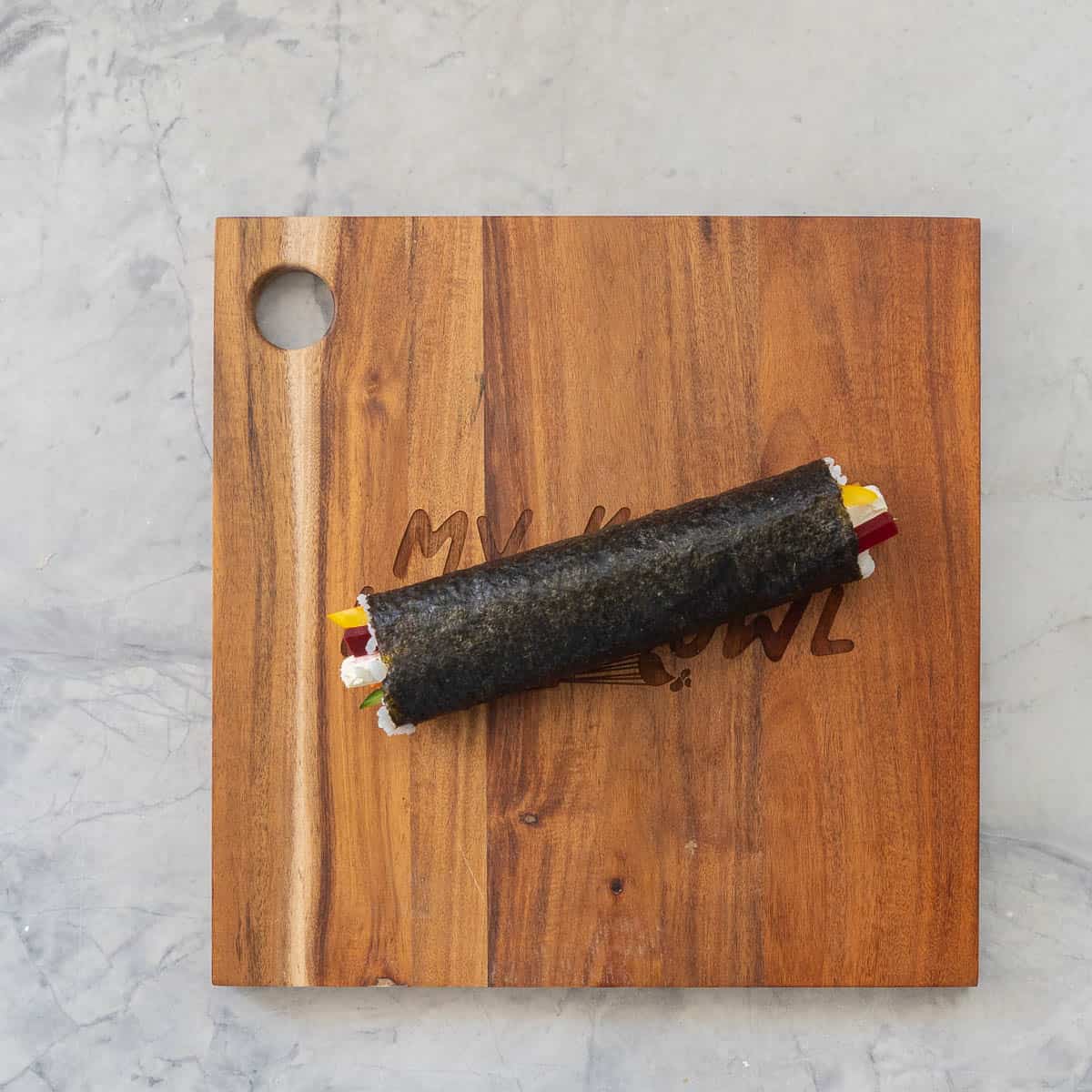 Sushi ingredients rolled into a long log on wooden chopping board.