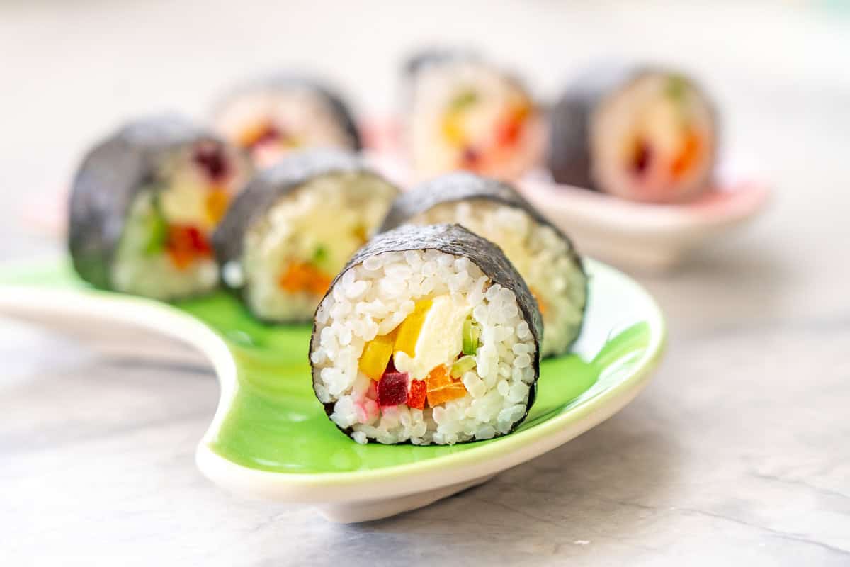 Piece of Rainbow Sushi on a plate showing ingredients inside.