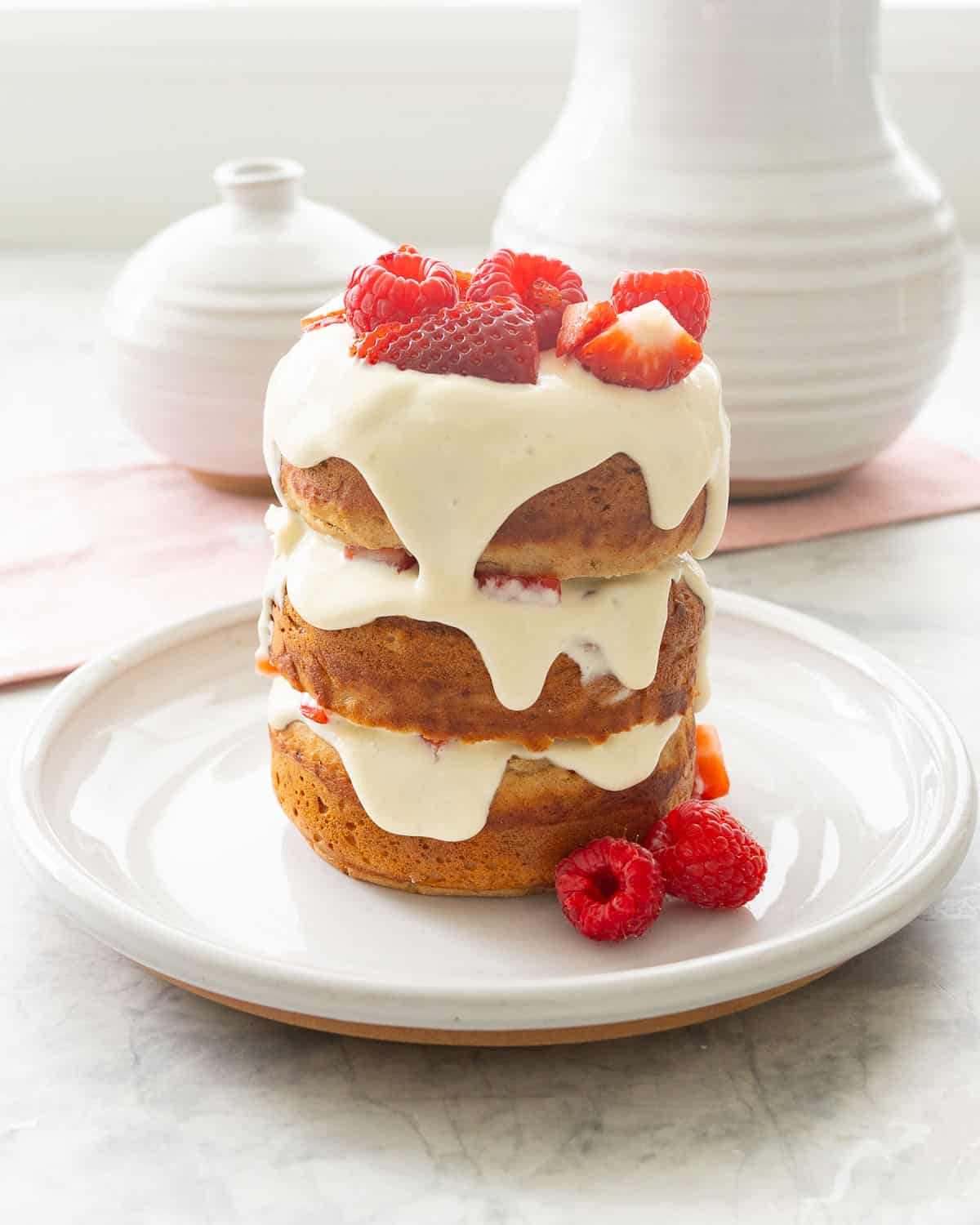 Three tier Smash cake layered with cream cheese, strawberries and raspberries with frosting drizzling down the sides topped with raspberries and strawberries.