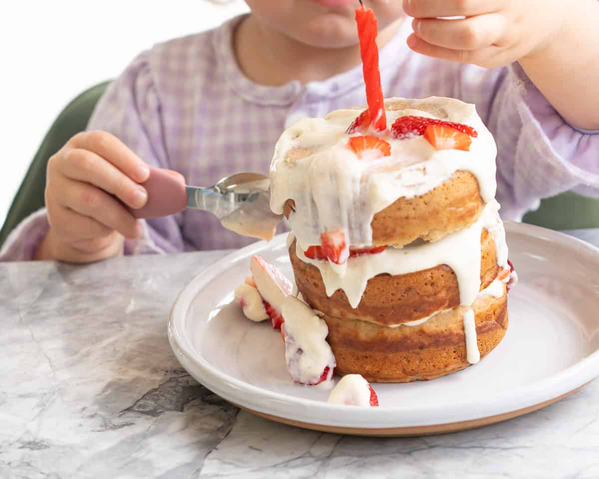 Three tier Smash cake layered with cream cheese, fresh strawberries and raspberries with frosting drizzling down the sides. A baby holding a spoon in one hand and the other taking fresh raspberries and strawberries off the top.