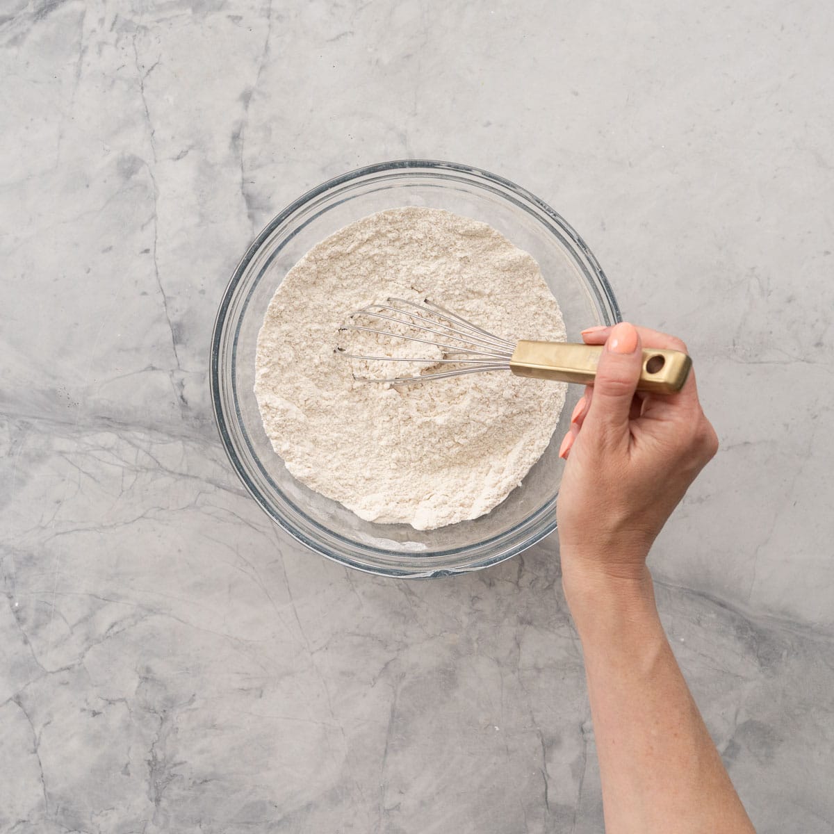 Dry Ingredients for Smash cake in a glass bowl on bench top being stirred with a whisk.