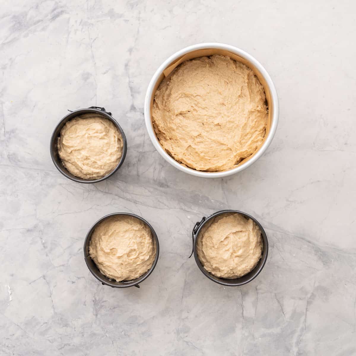 Smash Cake batter in three small cake tins and one large on benchtop.