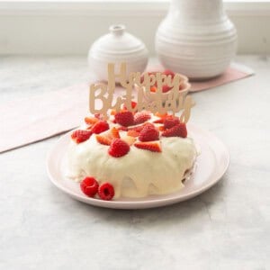 Smash Cake served on a blush pink plate, topped with frosting and garnished with halved strawberries, raspberries and topped with "Happy birthday" sign.