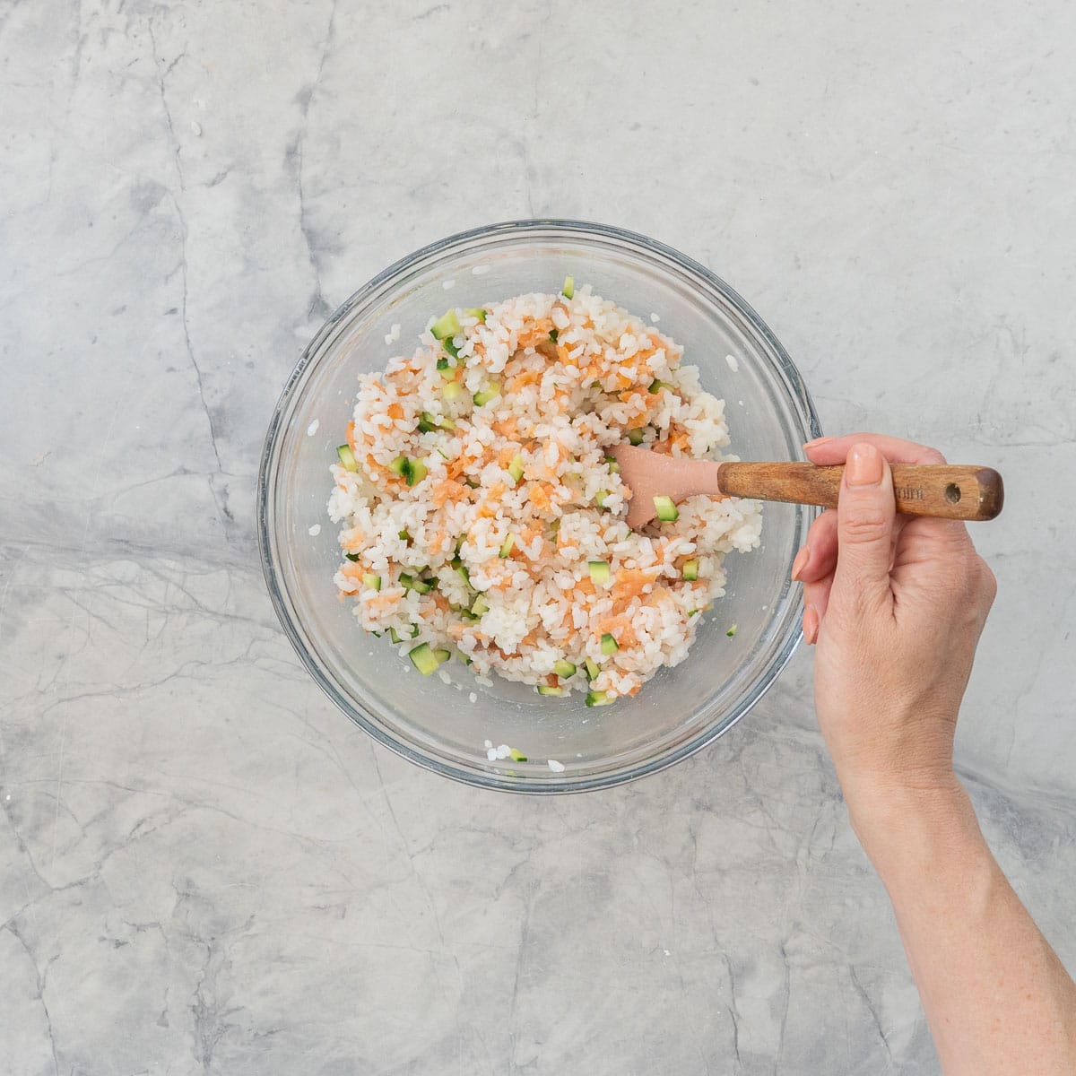 Diced cucumber, cooked sushi rice and diced salmon pieces in a big glass bowl mixed together with spatula.