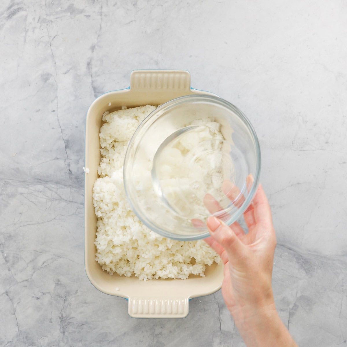 Vinegar Mixture being poured over a shallow dish of cooked rice.