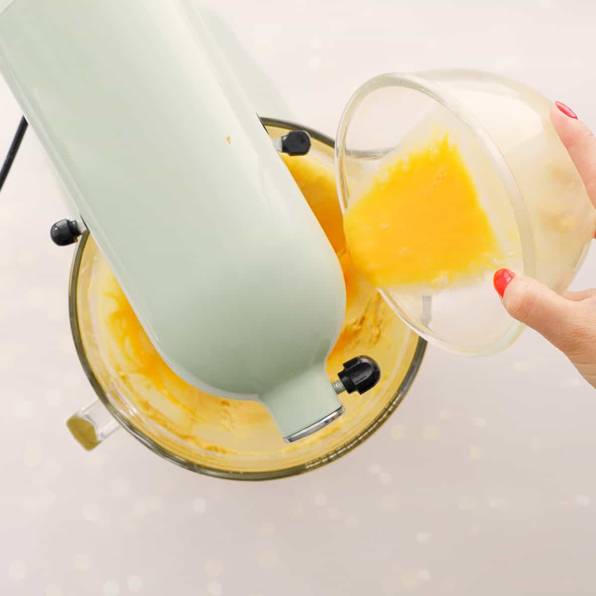 Egg yolks in glass bowl being poured into the wet ingredients whilst blender is mixing.