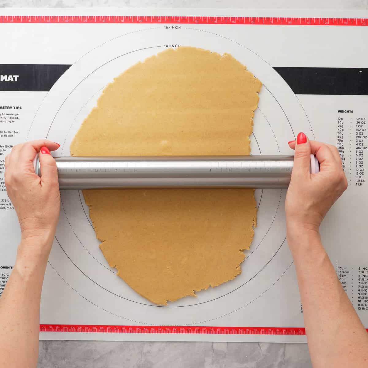 Hands holding a steel rolling pin rolling out GF Gingerbread dough onto 5mm thick.