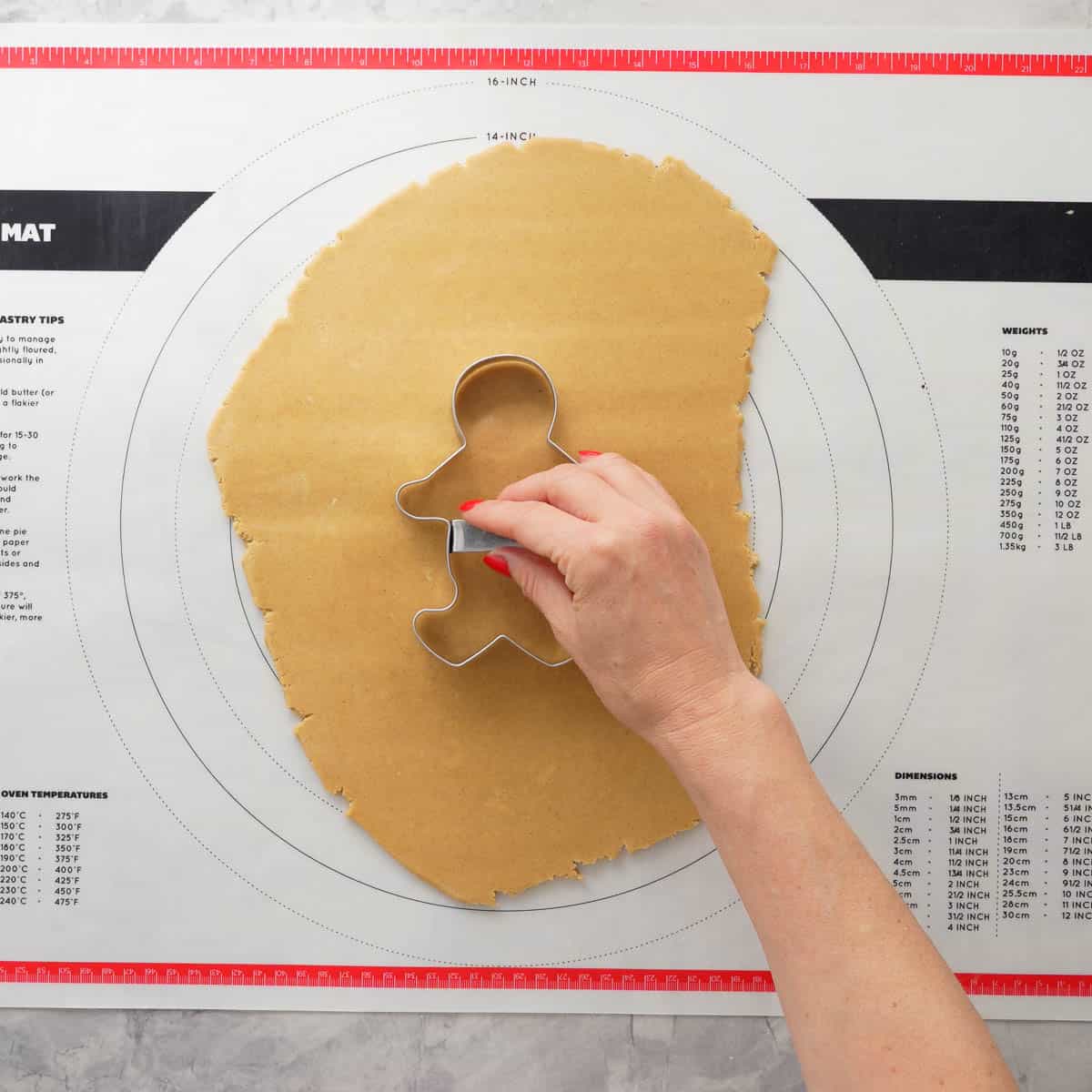 Hand holding a gingerbread cookie cutter on top of rolled out dough.