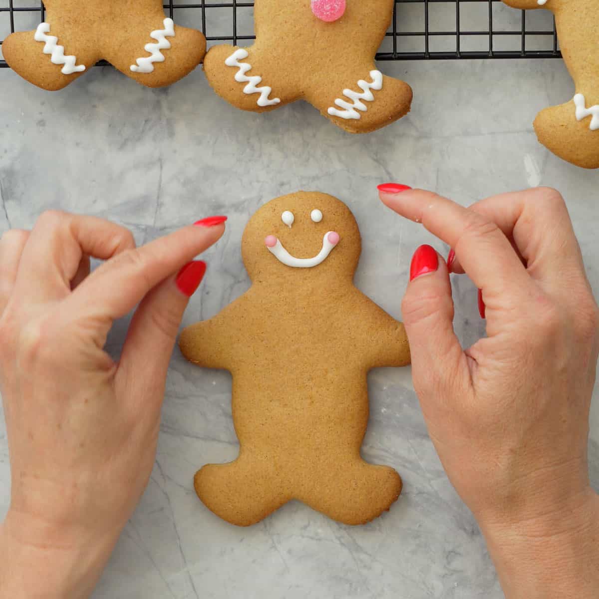 Fingers placing two light pink sprinkle balls on edges of royal icing smile on GF Gingerbread.