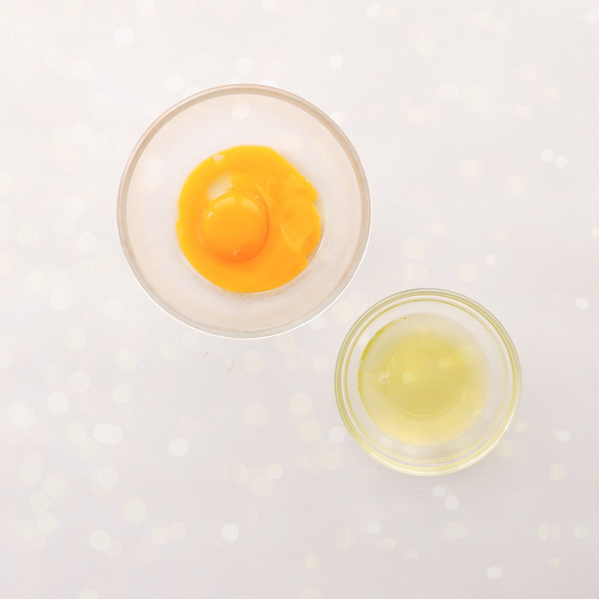 Two small glass bowls on bench top, one with egg yolk and one with egg white inside.