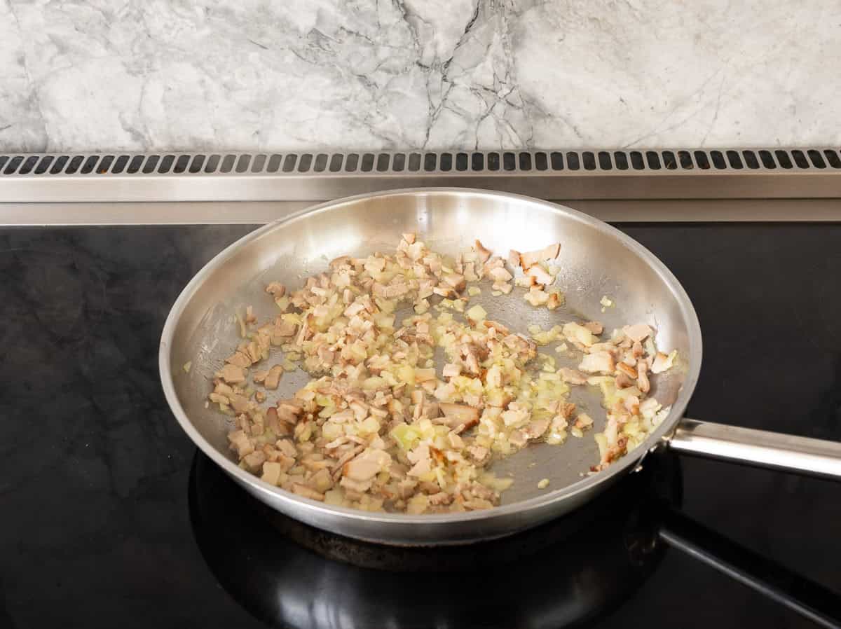 Onion, garlic and bacon in frying pan sautéing.