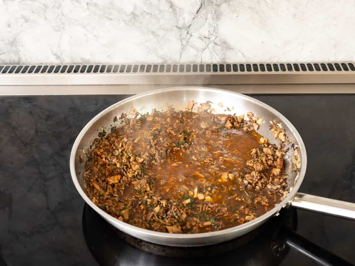 Beef broth, passata and chopped spinach added into pan on stove top with ground mince, grated mushrooms, onion, garlic and bacon in frying pan.