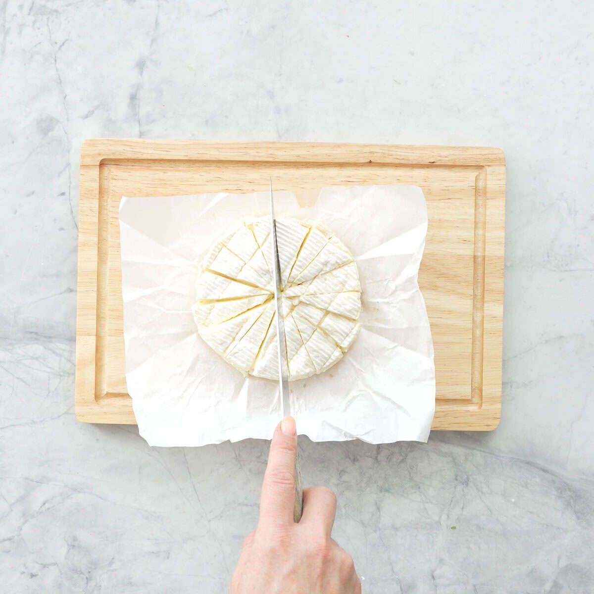 Knife cutting brie cheese into small wedges on chopping board.