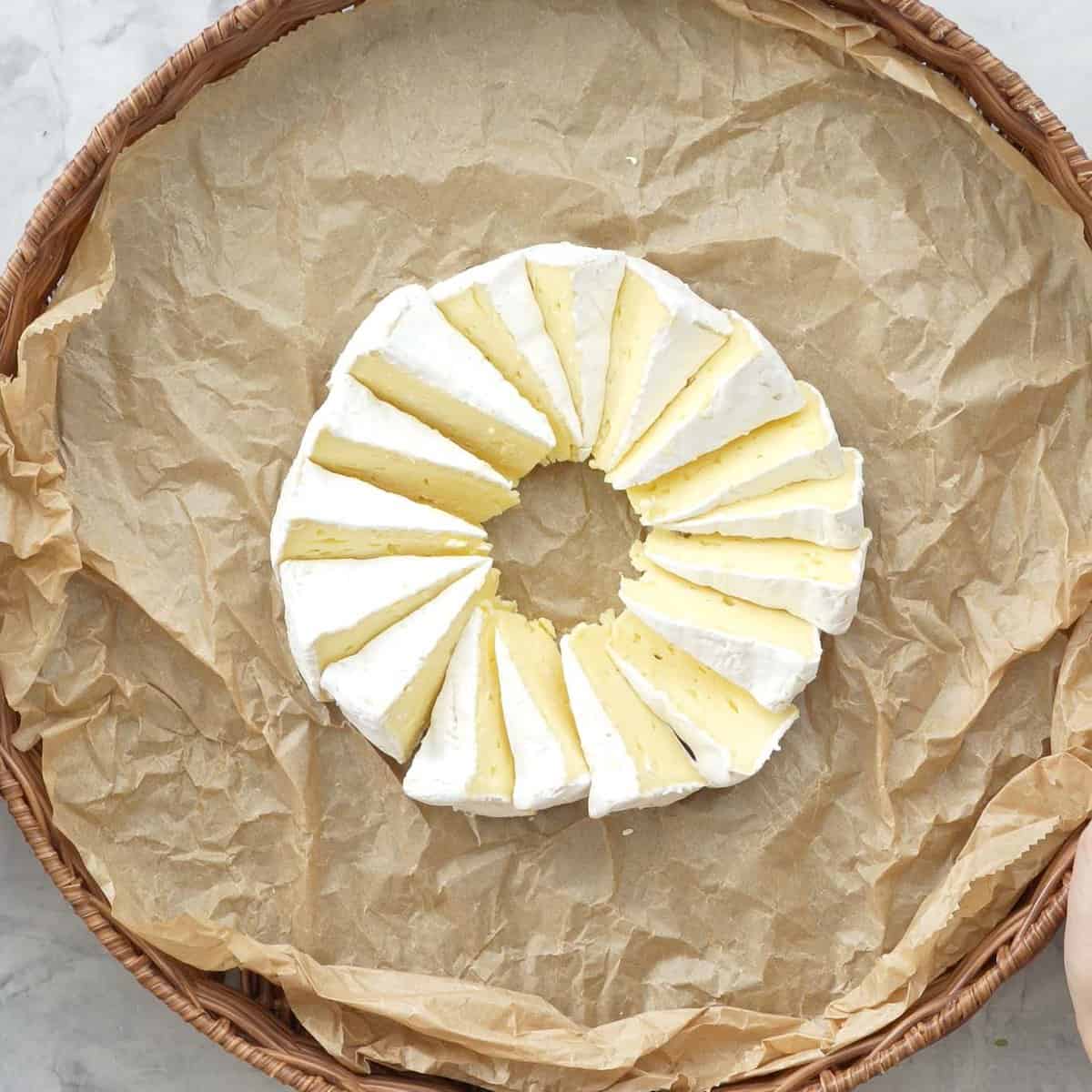 A circle platter board with parchment paper inside, Brie cheese cut into wedges and placed in the centre of board.