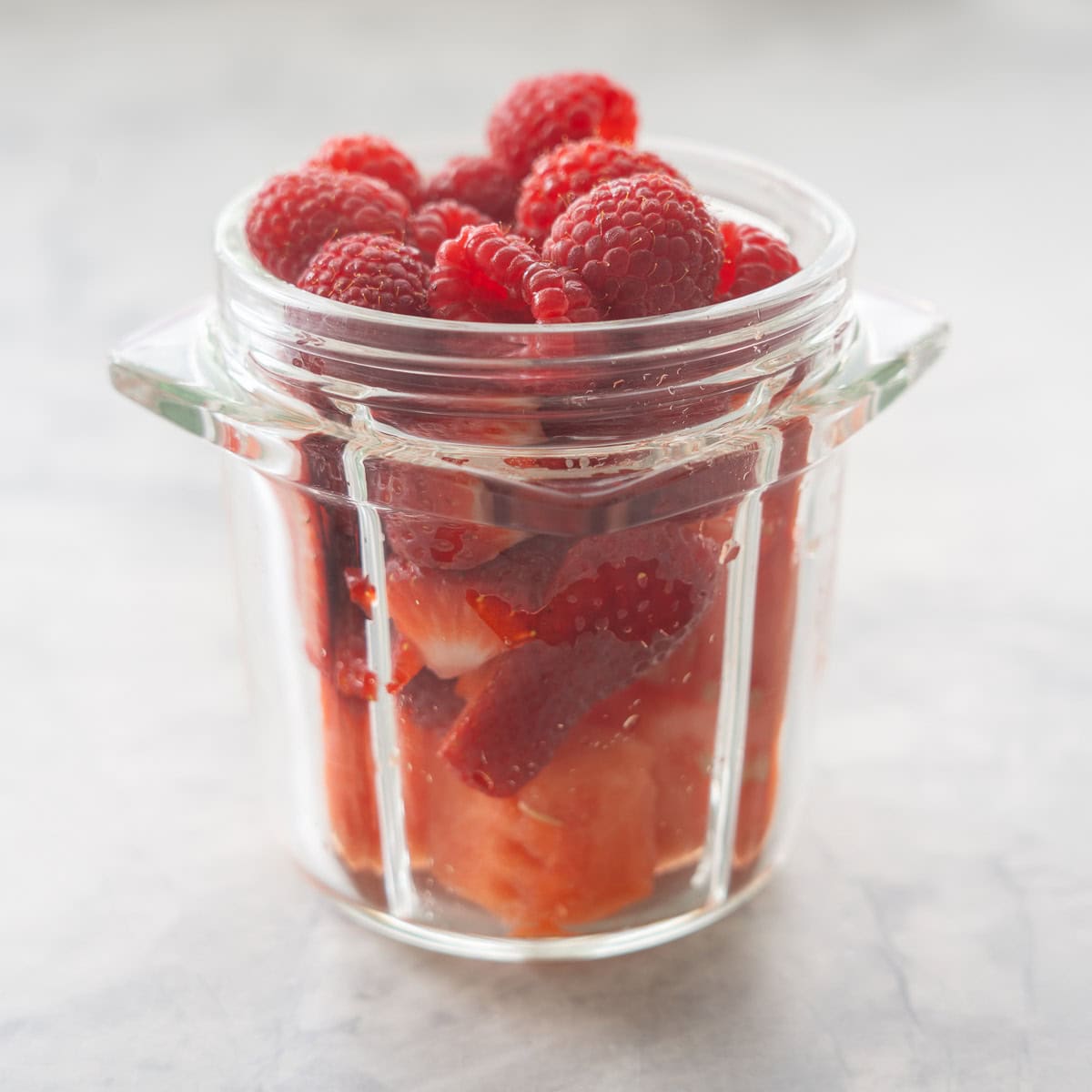 Watermelon, strawberries and raspberries in a smoothie cup on bench top.