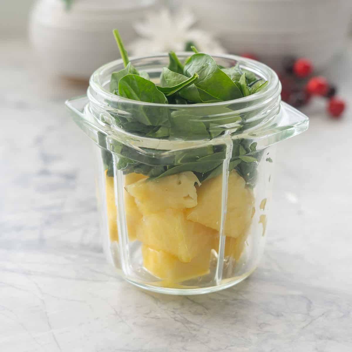 Pineapple, spinach and lemon juice in smoothie cup on benchtop.