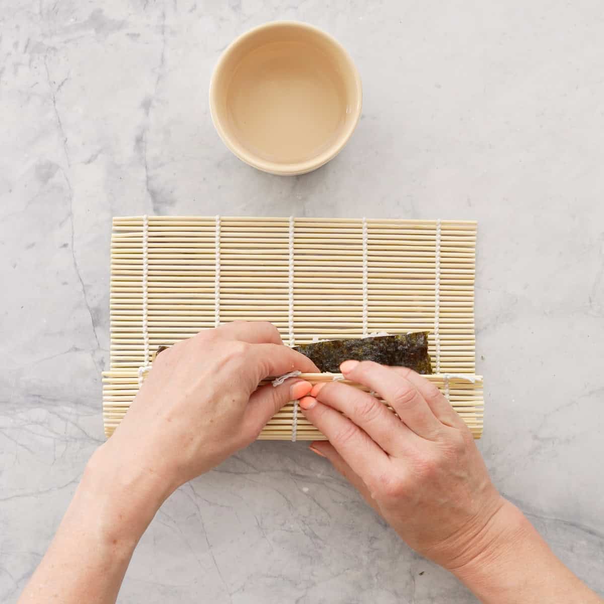 Hands holding sushi mat and rolling sushi up.