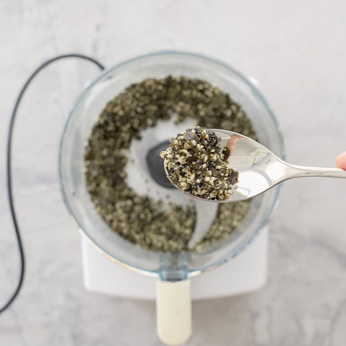 Spoonful of Furikake, nori and toasted sesame seeds blended up, with food processor and furikake below.