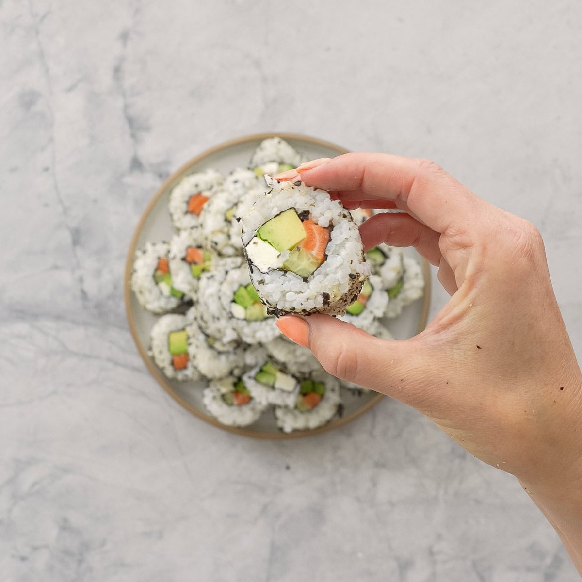 Hand holding a piece of Christmas sushi up to the camera showing fillings inside, cream cheese avocado, cucumber and salmon.