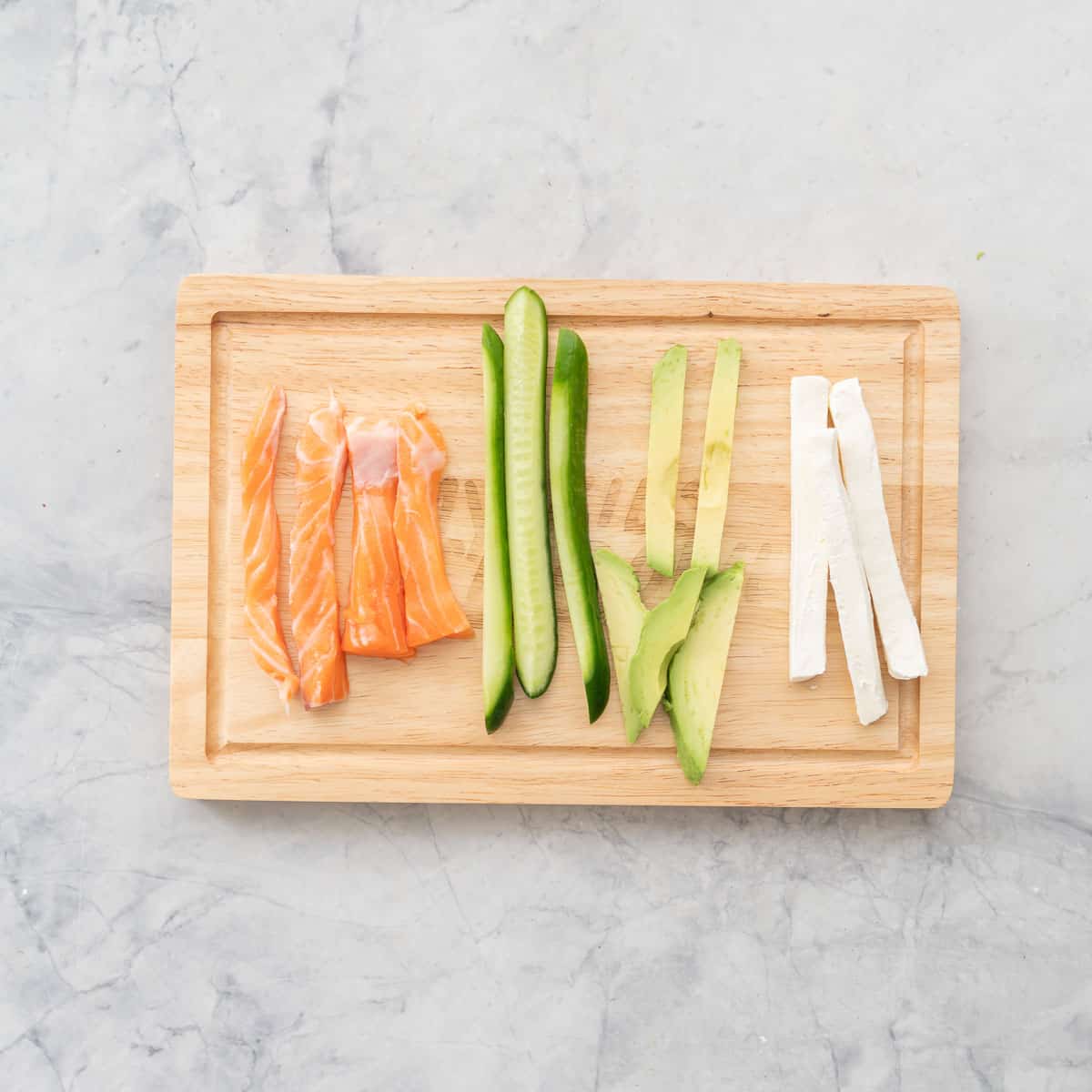 Ingredient fillings sliced Salmon, cucumber, avocado and cream cheese for Christmas sushi on wooden chopping board on bench top.