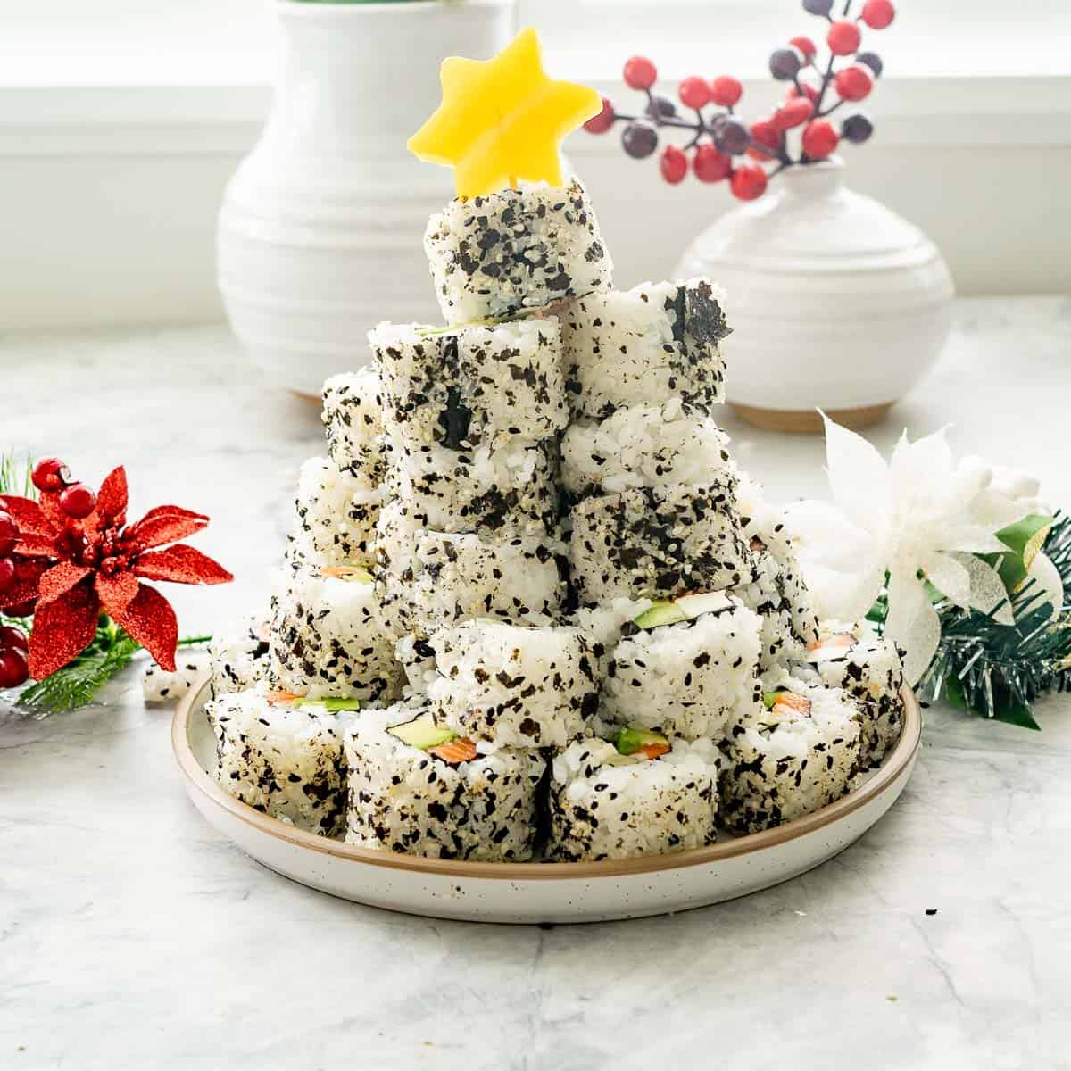 Stack of Christmas sushi on a plate with a yellow capsicum star cut out with toothpick stuck into the top of stack of sushi.